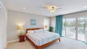 Une chambre avec un lit, un ventilateur de plafond, une fenêtre avec des rideaux et un balcon.