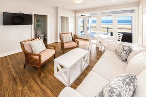A living room with a white sofa, two wooden chairs, a white coffee table, and a TV mounted on the wall.
