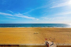Ein Strand mit blauem Himmel, sandigem Ufer und einem Steg mit einem Rettungsturm.