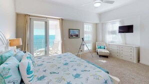 A bedroom with a bed, a TV, a balcony, and a ceiling fan. - Oceanfront, 2-story penthouse with 3 balconies, 3 pools & 2 gyms (Virginia Beach)