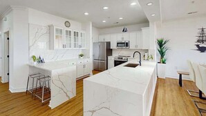 A modern kitchen with white cabinetry, a marble island, stainless steel appliances, and a dining area with a white table and chairs. - Oceanfront condo with gorgeous views, fast WiFi, washer/dryer, on-site pool/gym (Virginia Beach)