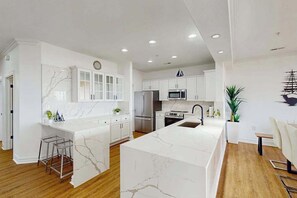A modern kitchen with white cabinetry, a marble island, stainless steel appliances, and a dining area with a white table and chairs. - Oceanfront condo with gorgeous views, fast WiFi, washer/dryer, on-site pool/gym (Virginia Beach)