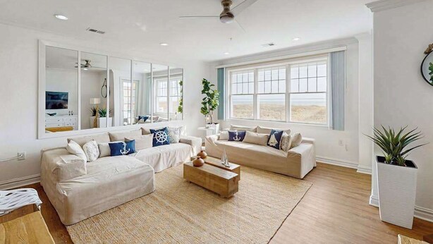 A spacious living room with a large window, a ceiling fan, and a wooden coffee table. - Oceanfront condo with gorgeous views, fast WiFi, washer/dryer, on-site pool/gym (Virginia Beach)