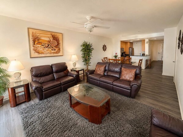A living room with two leather sofas, a glass coffee table, a ceiling fan, and a dining area in the background. - Your Perfect Family Beach Escape – Steps to the Sand with Resort-Style Amenities (Virginia Beach)