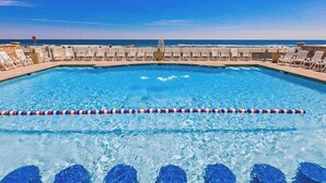 A swimming pool with a view of the ocean, surrounded by lounge chairs and a lifeguard stand. - Your Perfect Family Beach Escape – Steps to the Sand with Resort-Style Amenities (Virginia Beach)