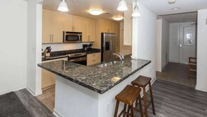 A modern kitchen with granite countertops, stainless steel appliances, and wooden cabinets. - Your Perfect Family Beach Escape – Steps to the Sand with Resort-Style Amenities (Virginia Beach)