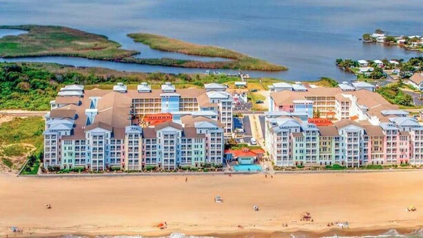 Ein Strandhotel mit mehreren Gebäuden, einem Sandstrand und Wasserflächen im Hintergrund.