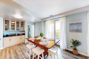 A dining area with a wooden table, white chairs, and a kitchen with open shelving. - Awesome home overlooking Back Bay with pool, washer/dryer & central AC (Virginia Beach)