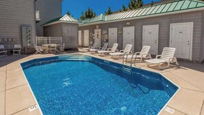 En swimmingpool med solstolar och en byggnad med numrerade dörrar.
