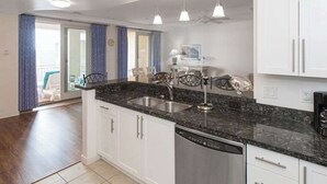 Een moderne keuken met witte kasten, een granieten aanrecht, een vaatwasser en hanglampen.