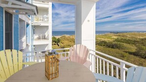 A balcony with a table, chairs, and a lantern; a view of the beach and dunes; and a white building with blue accents. - Luxury south-side condo with great views of the Atlantic/Back Bay, pools, & gym (Virginia Beach)