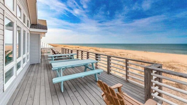 A wooden deck with picnic tables overlooking a beach. - Inviting oceanfront home with amazing views, private pool & deck (Virginia Beach)