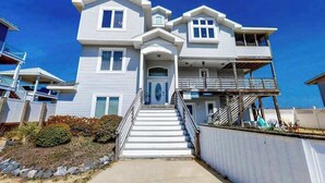 A two-story house with a front porch, a staircase leading to the entrance, and a balcony on the second floor. - Inviting oceanfront home with amazing views, private pool & deck (Virginia Beach)