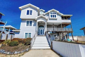 A two-story house with a front porch, a staircase leading to the entrance, and a balcony on the second floor. - Inviting oceanfront home with amazing views, private pool & deck (Virginia Beach)