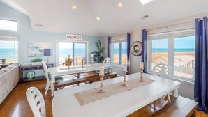 A beach-themed room with a dining table, chairs, and a view of the beach. - Inviting oceanfront home with amazing views, private pool & deck (Virginia Beach)