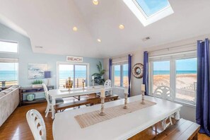 A beach-themed room with a dining table, chairs, and a view of the beach. - Inviting oceanfront home with amazing views, private pool & deck (Virginia Beach)