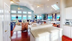A spacious living area with a kitchen island, multiple ceiling fans, and large windows offering a view of the ocean. - Inviting oceanfront home with amazing views, private pool & deck (Virginia Beach)