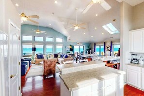 A spacious living area with a kitchen island, multiple ceiling fans, and large windows offering a view of the ocean. - Inviting oceanfront home with amazing views, private pool & deck (Virginia Beach)