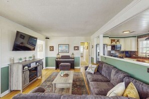 Ein Wohnzimmer mit Sofa, Couchtisch, Fernseher und einer Küchenzeile mit Schränken und Kühlschrank.
