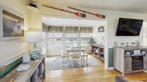 Una sala de estar con piso de madera, un comedor con mesa y sillas, un televisor montado en la pared y una chimenea.