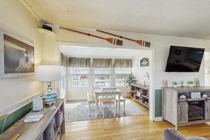 Ein Wohnzimmer mit Holzboden, einer Essecke mit Tisch und Stühlen, einem an der Wand montierten Fernseher und einem Kamin.