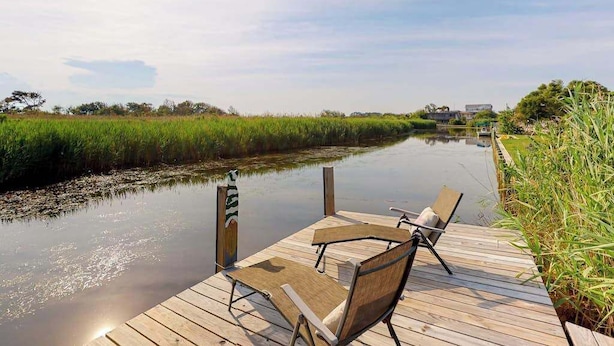 Un muelle de madera con dos sillas mirando a un río tranquilo, rodeado de vegetación.