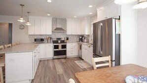 Une cuisine moderne avec des meubles blancs, des appareils en acier inoxydable et une table à manger en bois.