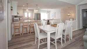 Une cuisine moderne avec des meubles blancs, un îlot central doté de chaises et des luminaires suspendus.