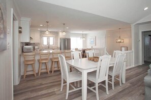 A modern kitchen with white cabinetry, a central island with chairs, and pendant lighting. - Oceanside beach house w/game room, pool & W/D (Virginia Beach)