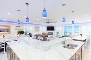 Een moderne keuken met een centraal eiland, hangende lampen, een plafondventilator en een groot raam met uitzicht op de oceaan.
