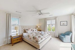 Une chambre à coucher avec un lit, une table de chevet, une chaise, un ventilateur de plafond et des fenêtres.