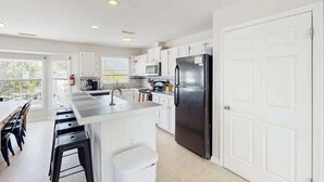 A modern kitchen with white cabinets, a black refrigerator, and a large window. - Well-Appointed Home w/Private Outdoor Pool, Gas Grill, Washer/Dryer, A/C (Virginia Beach)