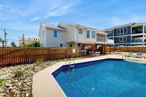 Ein Wohnhaus mit Swimmingpool, einer Holzterrasse und einem eingezäunten Garten.
