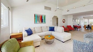 A spacious living room with a white sectional sofa, a round coffee table, and a dining area in the background. - Well-Appointed Home w/Private Outdoor Pool, Gas Grill, Washer/Dryer, A/C (Virginia Beach)