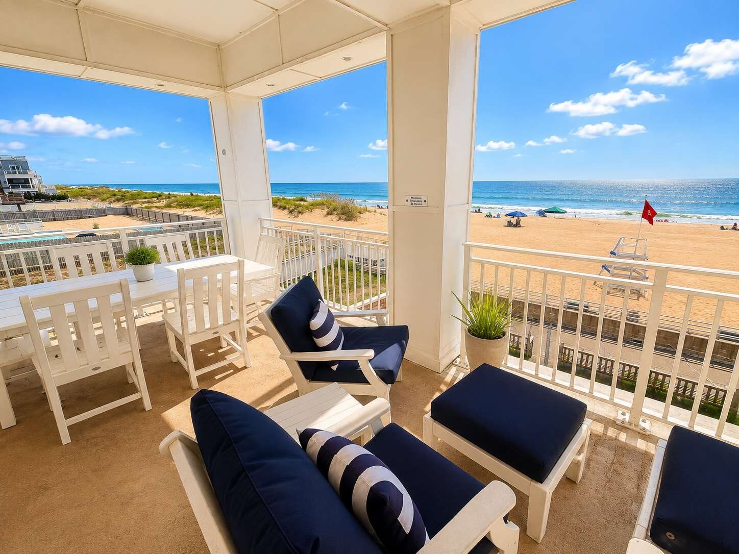 A covered outdoor seating area with white furniture and a view of the beach.