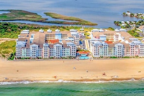 A beachfront hotel with multiple buildings, a sandy beach, and a water body. - Oceanfront corner condo with incredible views, balcony, pool, gym & AC (Virginia Beach)