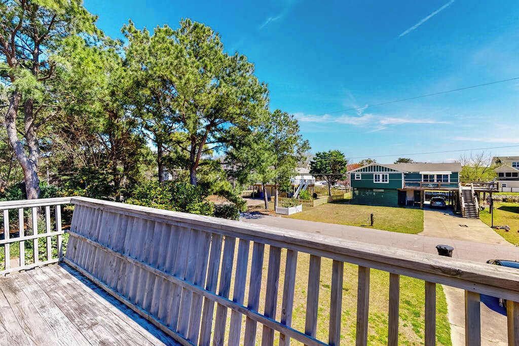 A wooden deck with a railing, a green house with a garage, and a grassy yard.