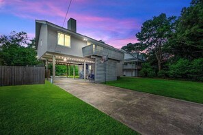 Ein zweistöckiges Haus mit überdachter Terrasse, sichtbarer Garage und gepflegtem Rasen.