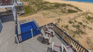Une vue sur la plage depuis une terrasse avec une piscine, des chaises et une clôture.