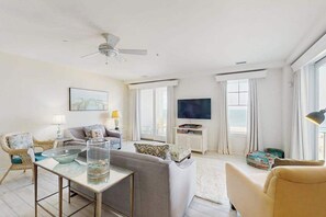 Ein Wohnzimmer mit Sofa, Sessel, Tisch, Fernseher und Deckenventilator.