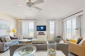 Ein modernes Hotelzimmer mit Balkon, Flachbildfernseher, Sofa, Couchtisch und Deckenventilator.