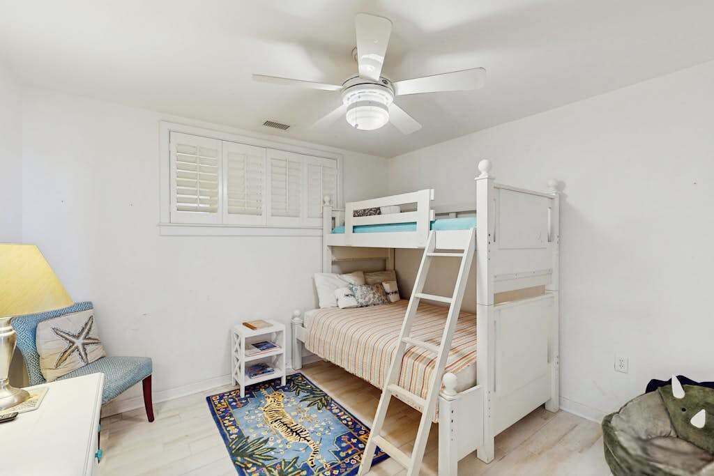 A child's bedroom with bunk beds, a ceiling fan, a small desk, and a starfish pillow.
