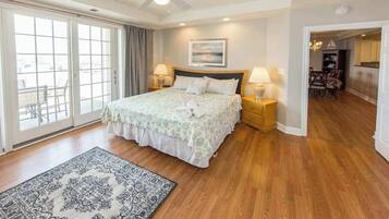 Un dormitorio con cama, dos mesitas de noche, ventilador de techo, ventana grande y vistas al exterior.