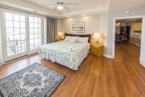 A bedroom with a bed, two bedside tables, a ceiling fan, a large window, and a view of the outside. - Southside condo with ocean view, easy beach access, fast WiFi & on-site pool/gym (Virginia Beach)