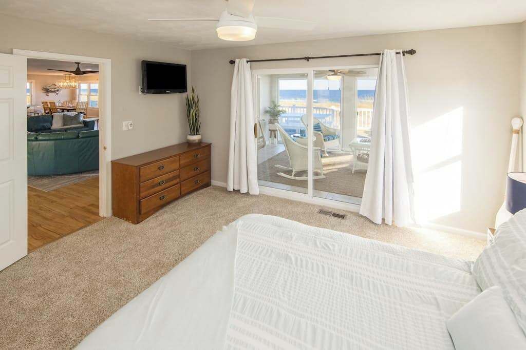 Een slaapkamer met een bed, een dressoir, een televisie en een balkon met gordijnen.