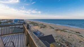 Een houten terras met uitzicht op een strand, onder een heldere lucht.