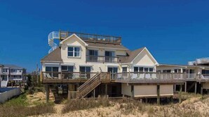 Een strandhuis met balkon, trap en terras.
