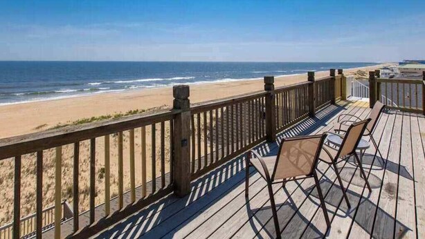Een houten terras met stoelen met uitzicht op een strand.