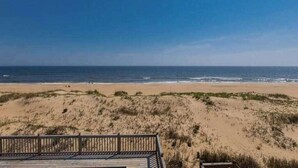 Uitzicht op een strand met een houten terras en duinen.