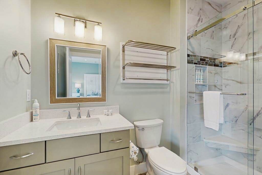 Une salle de bain équipée d’un lavabo, d’un miroir, d’un porte-serviettes, de toilettes et d’une douche à parois en verre.